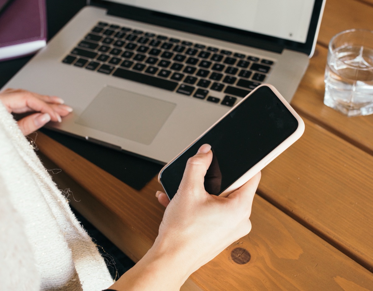 Figure 1.1: A hand holding a smartphone next to an open laptop on a wooden table.