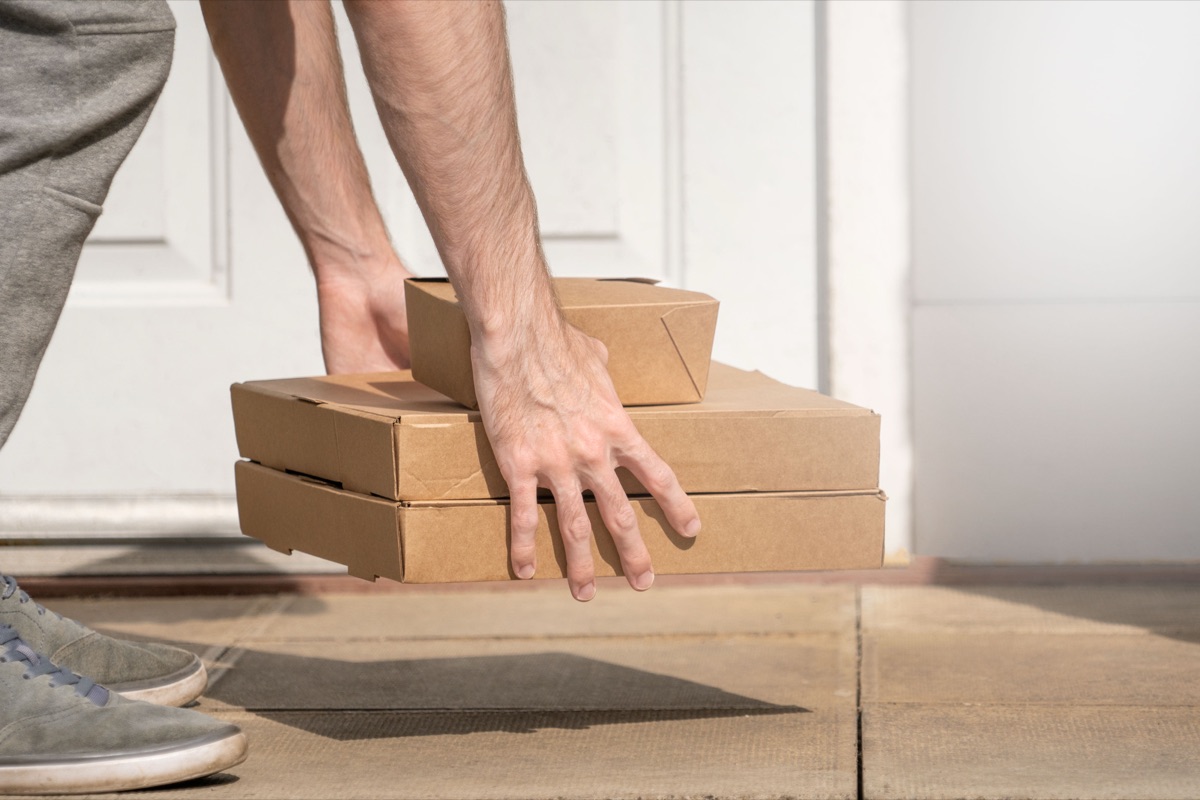 A delivery driver sets two takeout boxes down on a doorstep in front of a white front door
