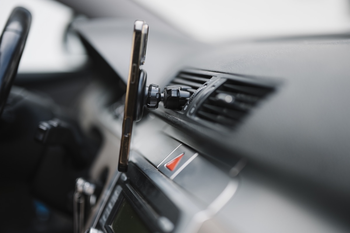A smartphone held in a magnetic mount on a car air vent next to the dashboard