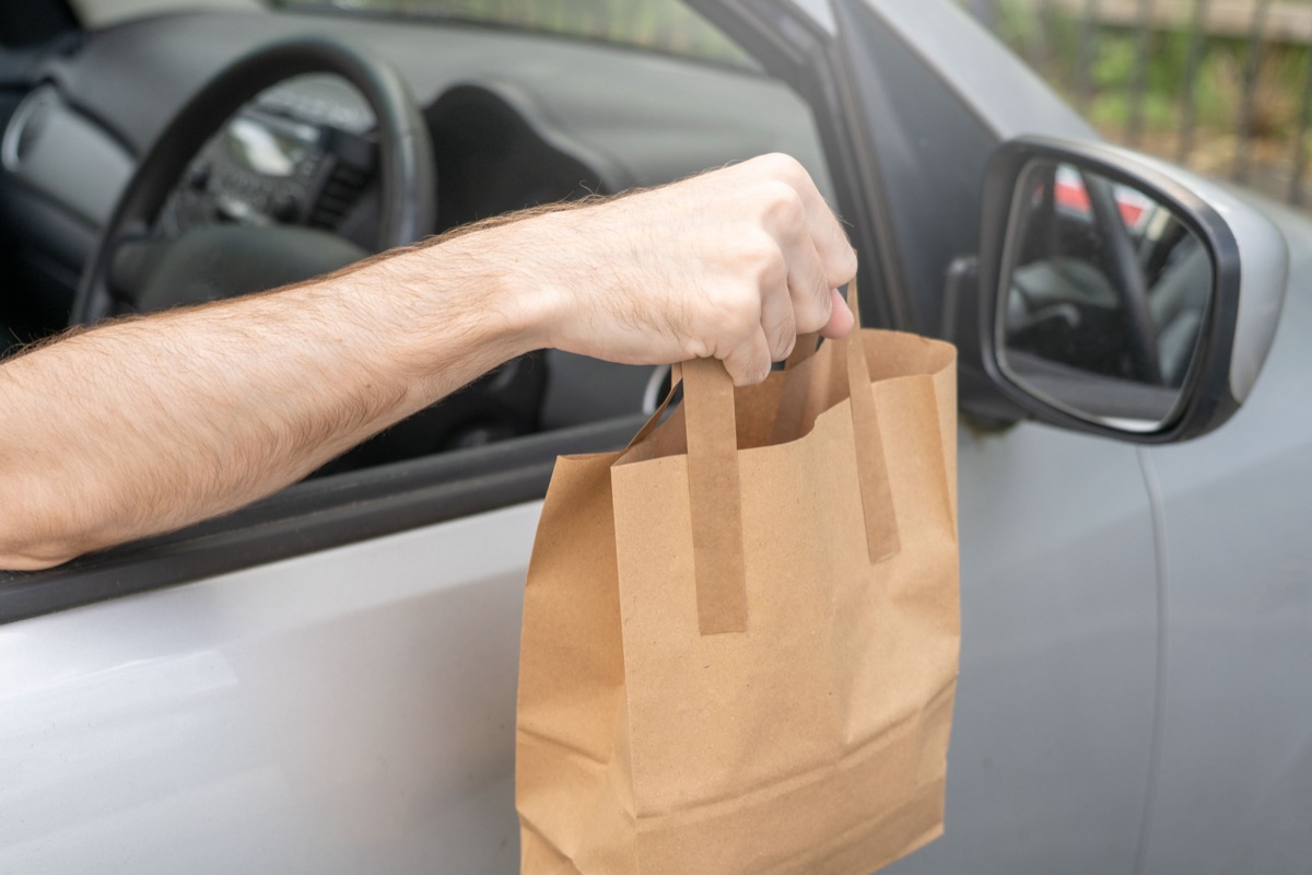 A driver's arm holding a paper takeout bag out of a car window