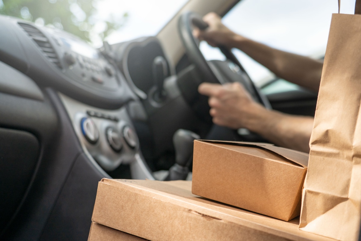 Takeout boxes and a paper bag on a car's passenger seat while the driver steers