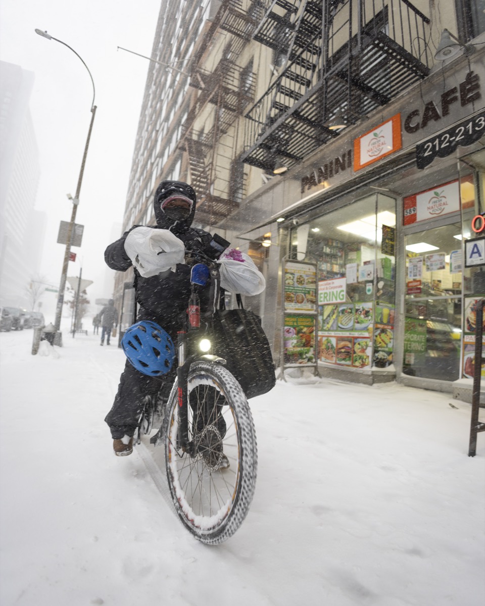 Figure 2.1: A bicycle courier in heavy snow on a Manhattan sidewalk, with bags hung on the handlebars and a helmet clipped to the bike.