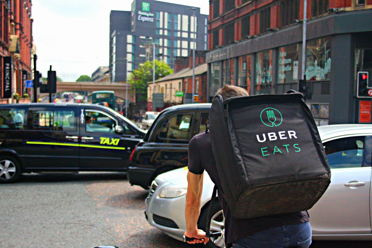 A cyclist with an Uber Eats delivery backpack rides between taxis and cars on a busy city road