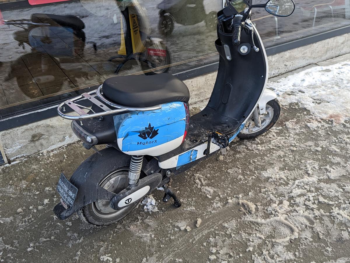 A small electric bike with a delivery rack parked on a slushy sidewalk outside a coffee shop window