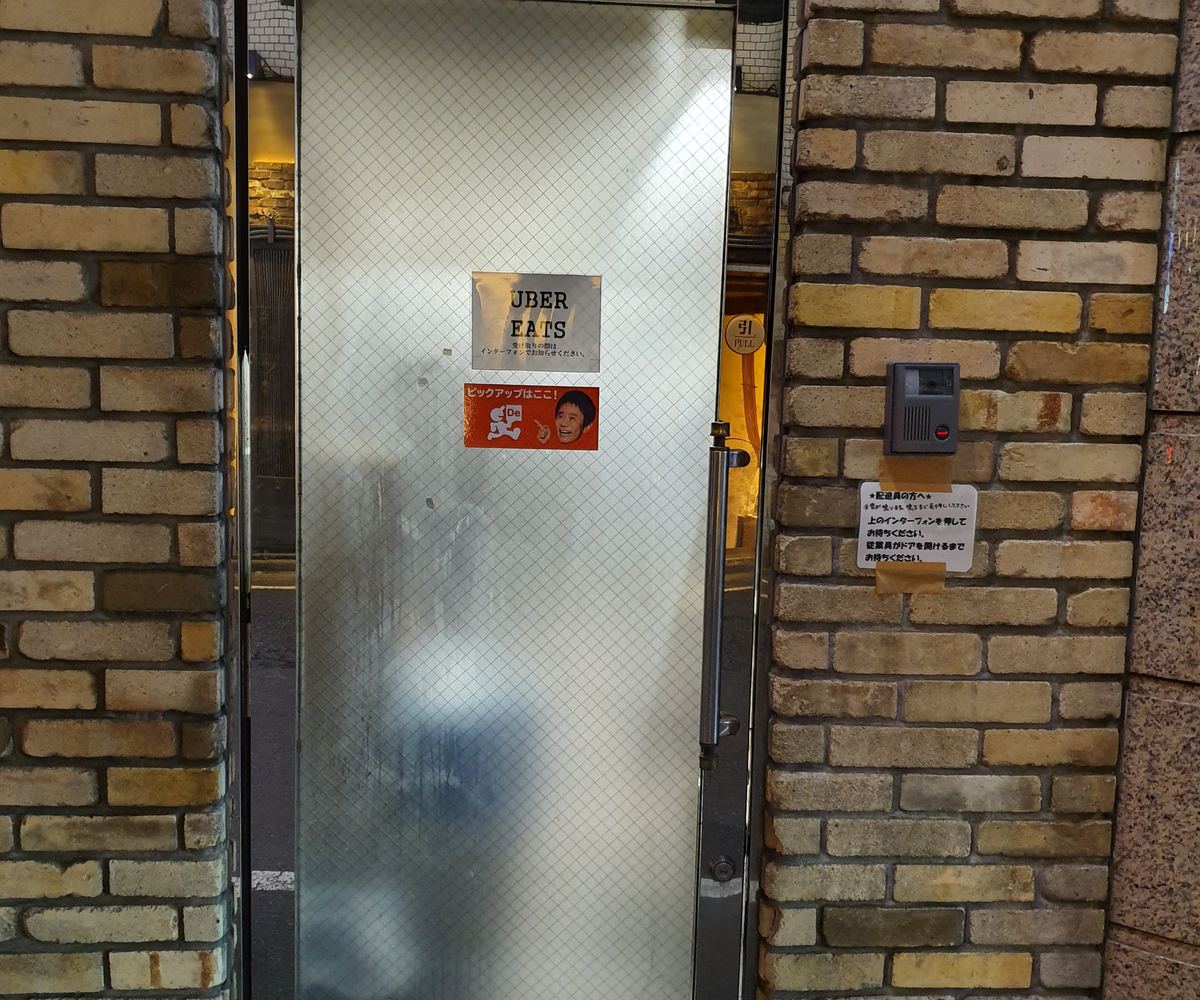 A frosted glass side door between brick walls with a small Uber Eats sign, used as a delivery pickup entrance